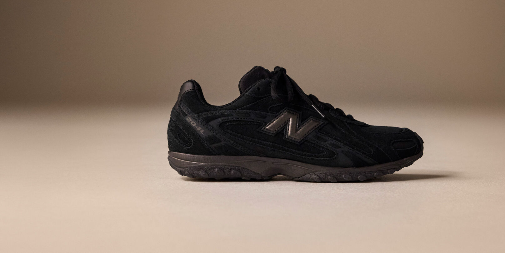 Side image of a black 204L sneaker on a brown background